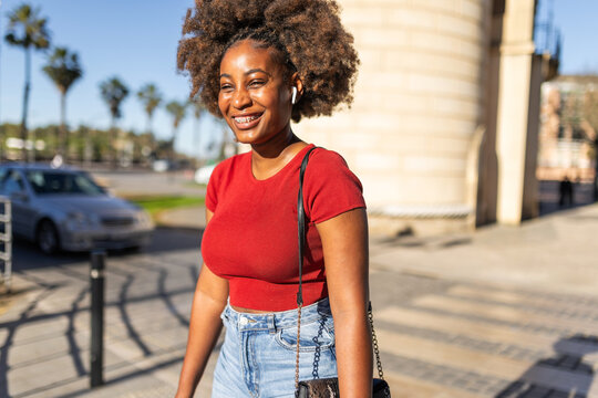 Black woman with headphones crossing the street on a sunny day.