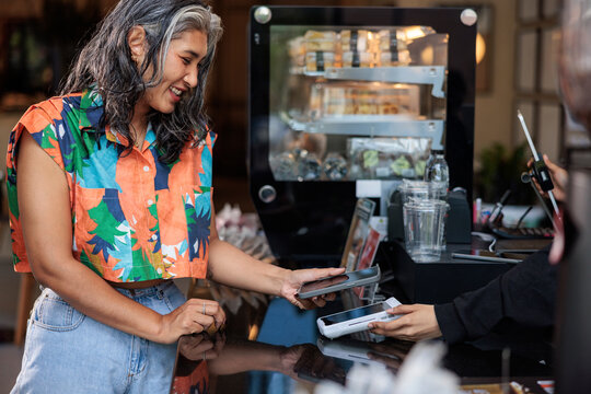 Woman paying with phone at cafe counter.