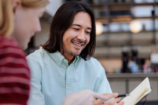 Two people collaborate, smiling, while looking at a notebook.