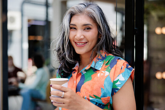 Smiling woman with coffee stands by a door.