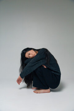 Person squatting hugging knees feeling alone