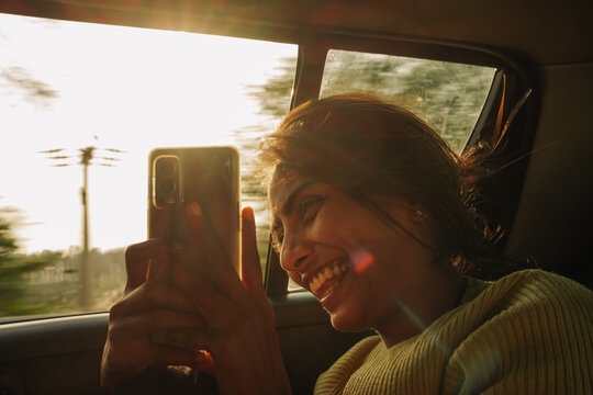 Smiling Woman Using Phone in Moving Car During Sunset