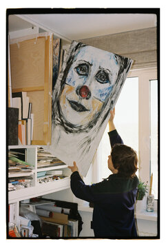A woman places a large painting on a shelf in an art studio.