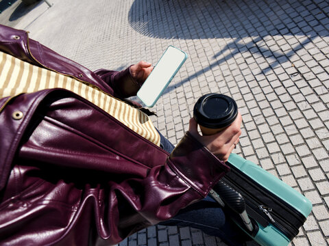 Traveler carrying suitcase, coffee and smartphone checking directions