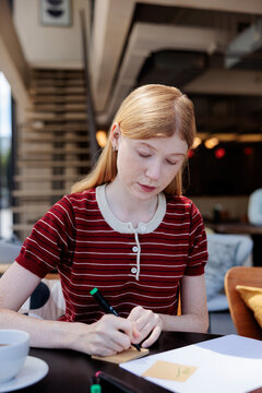Redhead woman writing on paper at a cafe.