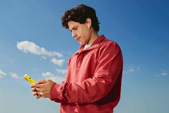 Man using smartphone outdoors with wireless earbuds