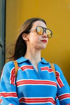 Confident woman in sunglasses against bold yellow wall
