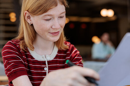Redhead woman reviews document with pen in hand.