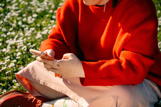 Person Sitting on Grass With Phone in Hand Wearing Bright Sweater
