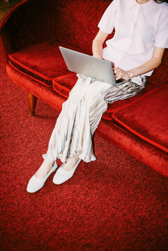 Business woman with laptop on red sofa in office, film photo 