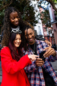 Group of friends in city street looking at smartphone smiling
