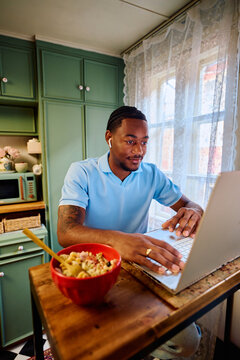 Young Black Man Working on Laptop at High Table in Kitchen