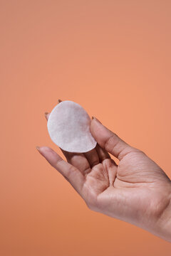 Woman's hand holding a white cotton pad against an orange background