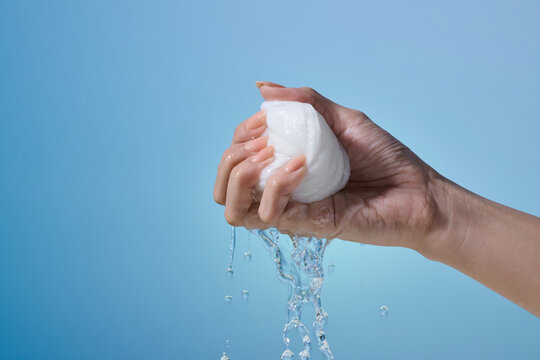 hand squeezing water from a white cloth against a gradient blue
