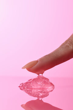 Finger touching a pink gel, with a reflection against a soft pink