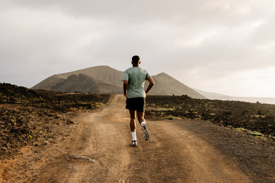 Far rear perspective of a trail runner training on a dirt road