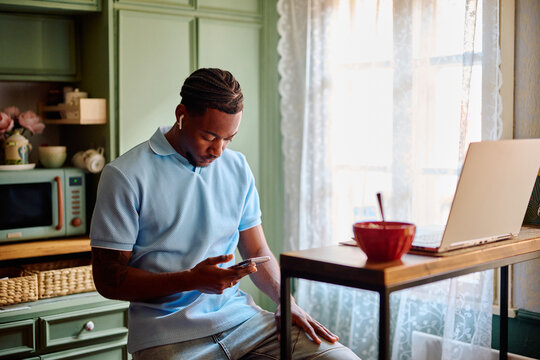 Young Black Man Checking Smartphone During Break in Kitchen