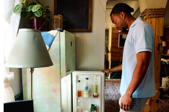 Young Black Man Looking for Food in Open Refrigerator at Home