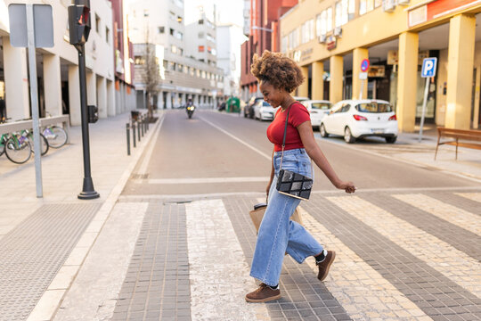 Black woman crossing the street with shopping bags, smiling