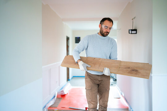 A man walks down a hallway carrying a wooden plank