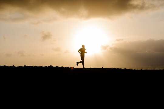 Silhouette of athletic man running along a dirt path in the hills