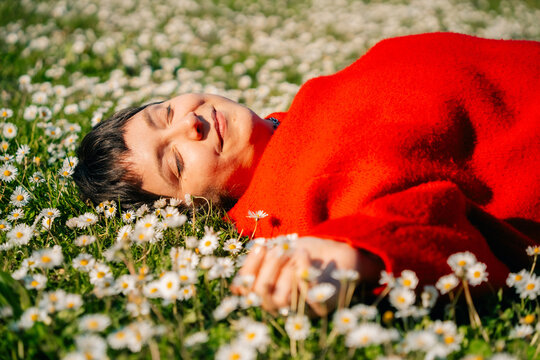 Person Relaxes on Grass Among White Flowers in Bright Red Sweater