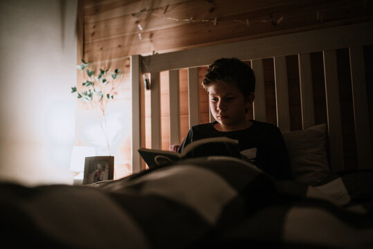 Boy reading a book at night in his bedroom.