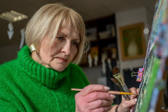 Elderly woman artist drawing on easel in workshop
