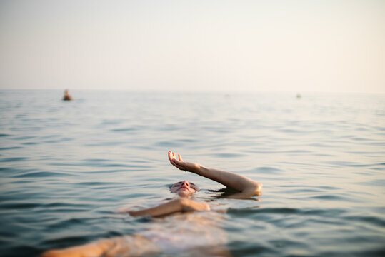 Woman floating in calm sea with raised arm at golden hour