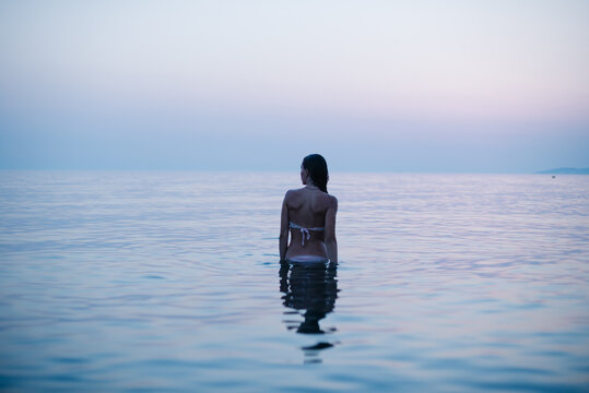 Woman standing alone in calm sea at blue hour