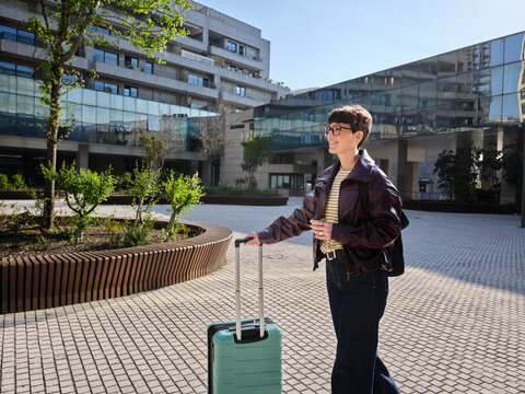 Young woman smiling, walking with suitcase in urban setting