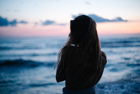 Woman with long hair facing ocean at blue hour