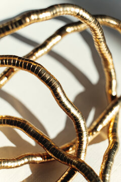 Gold Metal Wire Shapes on a White Surface in Bright Light