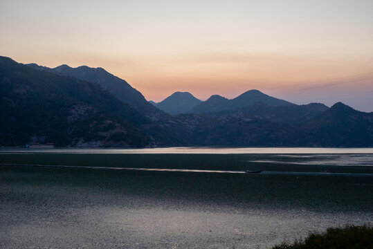Motorboat trail across a calm lake with layered mountains at sunset