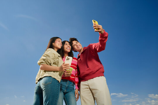 Friends posing for group selfie outdoors under blue sky
