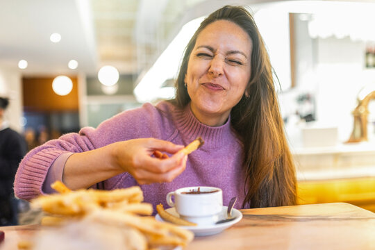 Playful woman winking while eating churros with chocolate