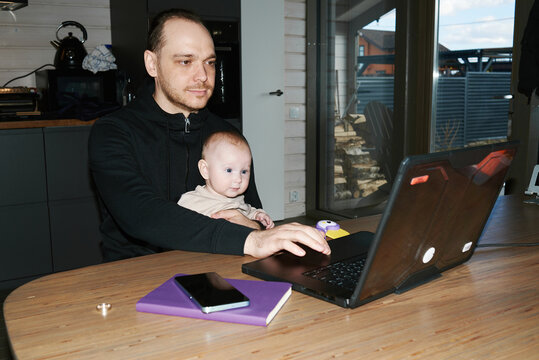 Father works on laptop with baby in his lap