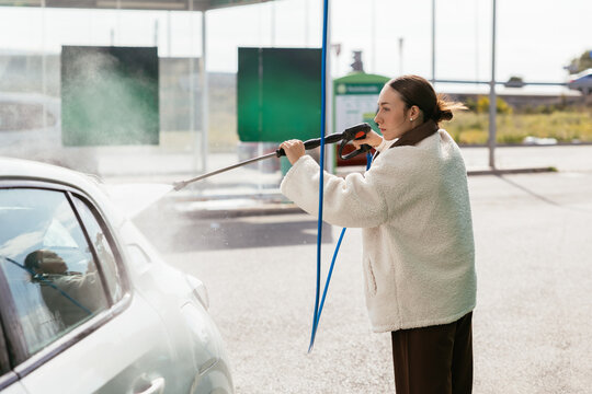 Woman washing white car with high pressure water