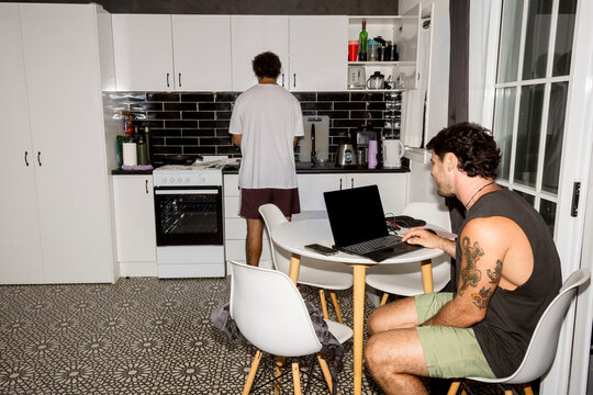 UGC Man using laptop while friend cooks in home kitchen