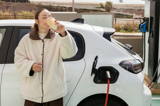 Woman drinking coffee while charging electric car
