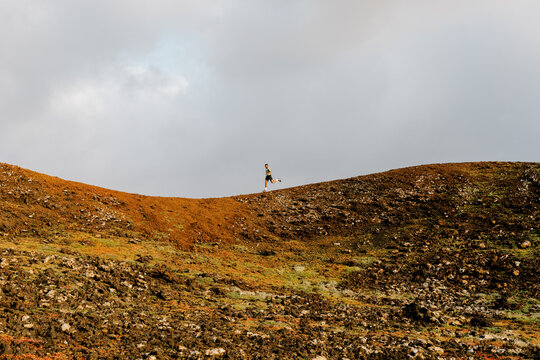 Wide view shows a trail runner far away training along a rocky path