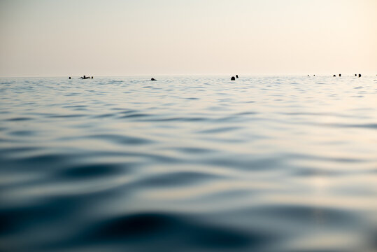 Calm blue sea with swimmers at sunset