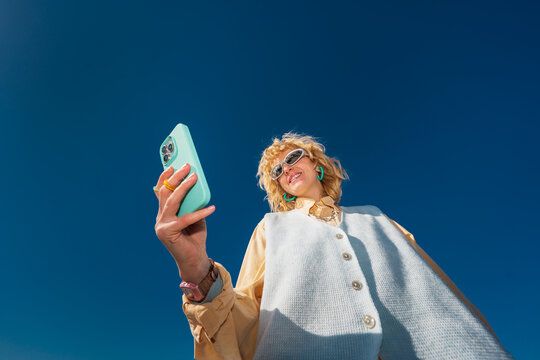 Low angle portrait of smiling woman taking selfie outdoors