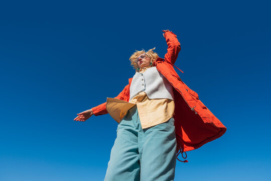 Low angle view of dancing woman with flowing coat outdoors