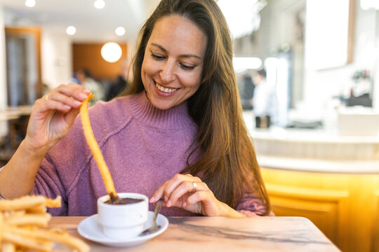 Happy woman enjoying traditional Spanish churros and chocolate