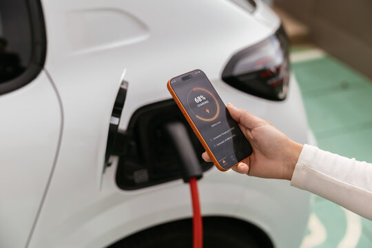 Hand using smartphone application monitoring electric car charging