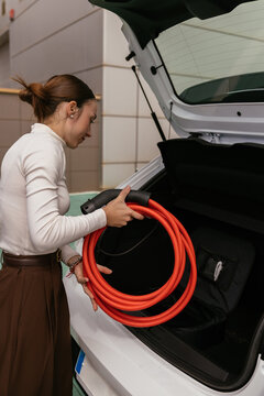 Woman handling electric car charging cable in trunk