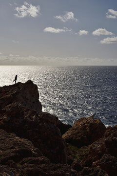 Silhouette on rocky ridge facing open sea in soft wind
