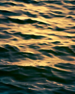 high angle close up of the ripples of water of a sea at summer sunset. sunlight shines on the soft surface of ocean at hot weather.