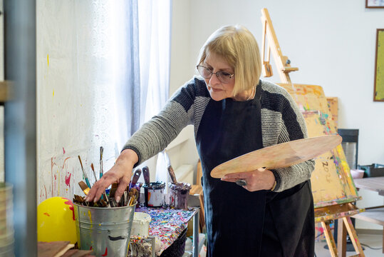 Elderly female artist picking up paint on palette in workshop